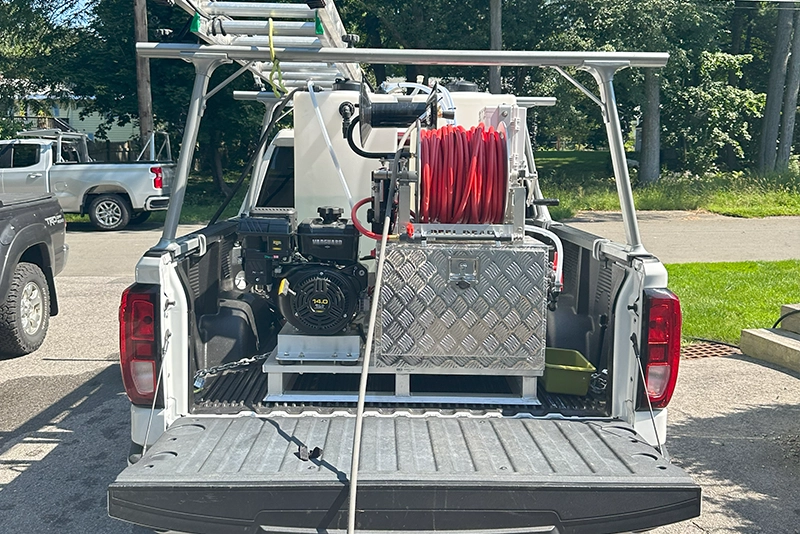 A pickup truck bed showing equipment including a water tank, hoses, and a pump, ready for maintenance tasks. 