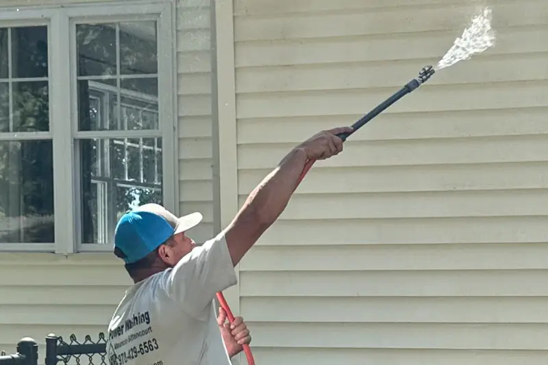A person is pressure washing the vinyl siding of a house.